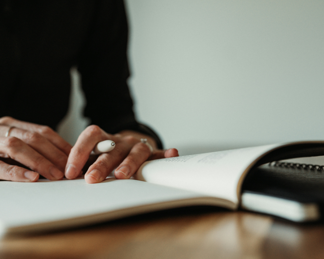 person with pen and notebook sitting at a table